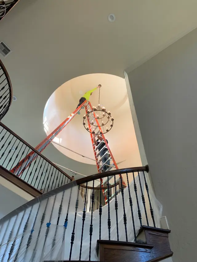Electrician on a tall ladder hanging an iron chandelier in a curved two-storey stairwell