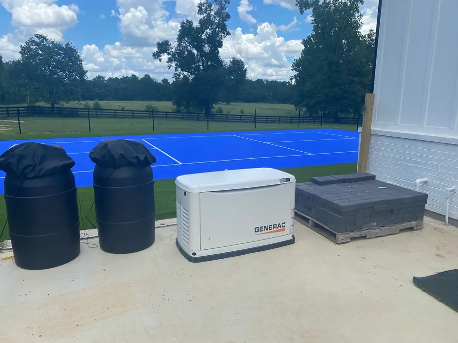 Standby generator on a concrete pad beside a sport court and open pasture